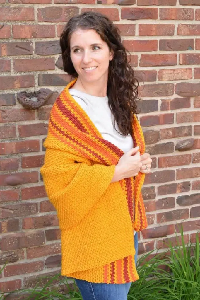 Smiling woman wrapped in a marigold crochet prayer shawl with pumpkin and burgundy stripes