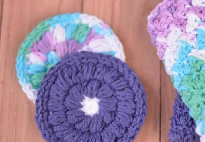 Two crochet face scrubbies stacked. One ombre and one purple flower.