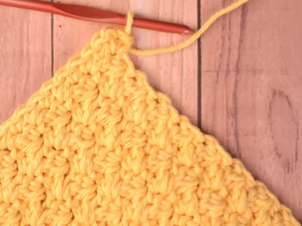 Yellow crochet washcloth with a border of single crochet stitches being added