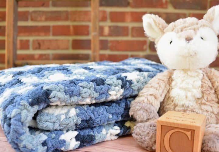 Blue variegated yarn baby blanket with a grey stuffed fox and wooden letter block.