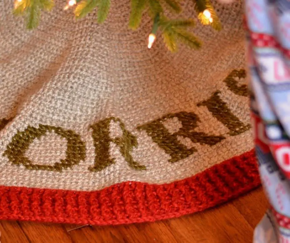 Rustic Christmas tree skirt that is crocheted in grey yarn, with a red ribbed border, and monogramming in green letters