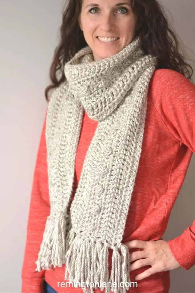 Woman in a strawberry long sleeve shirt wearing a marbled grey scarf with bobble texture and fringe