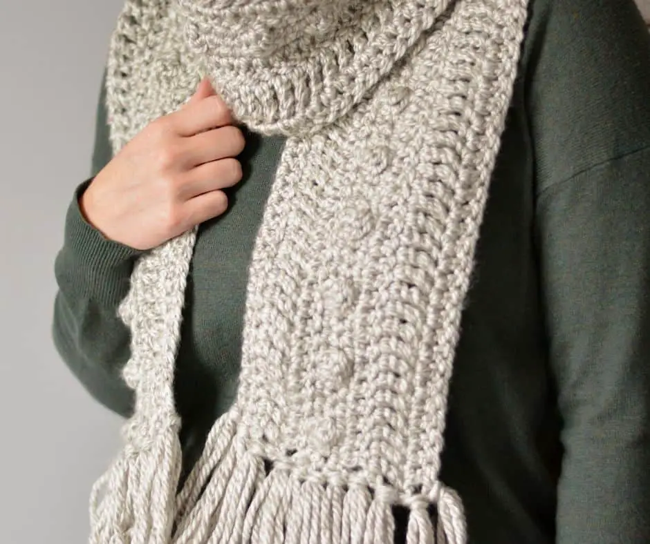 Woman wearing grey textured scarf and green sweater.