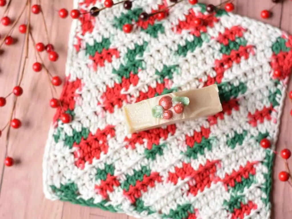 Holly berry handmade soap on top of a red, white and green variegated crochet washcloth