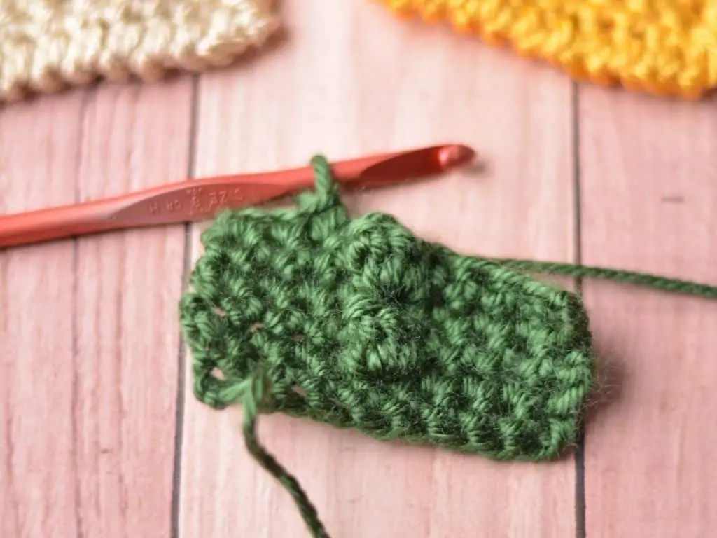 A close-up of a green crochet pocket prayer square that is partially made