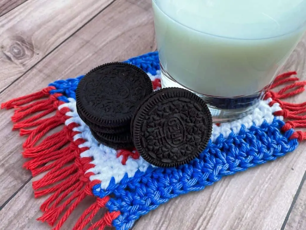 A USA coaster made from red, white, and blue yarn with a glass of milk and Oreo cookies on top