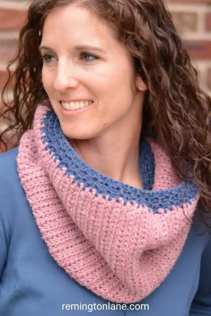 A closeup of a woman's cowl that is crocheted in heathered rose pink yarn and dark blue trim.