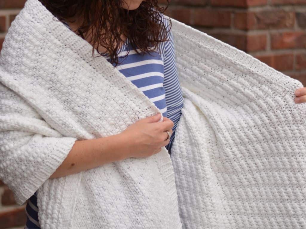 A woman in a blue and white striped shirt, wrapped in a textured shawl made from white yarn.