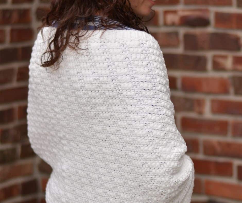 The back view of a woman wearing a textured white cozy shawl