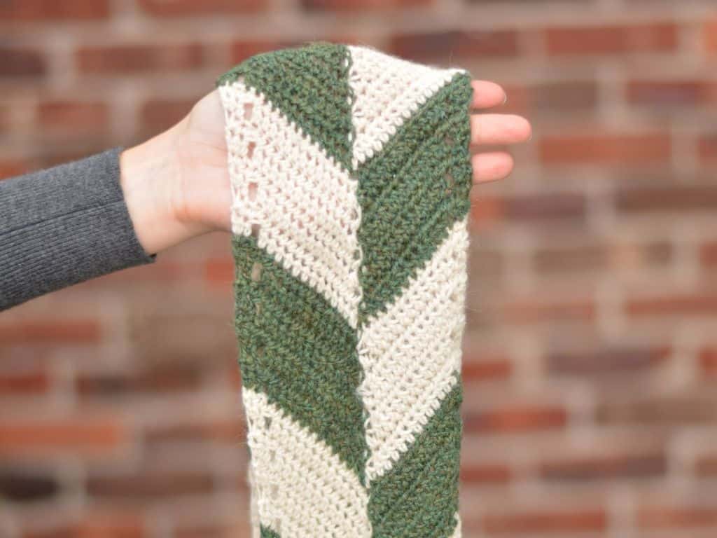 A hand with a narrow multi-colored crochet scarf draped over it