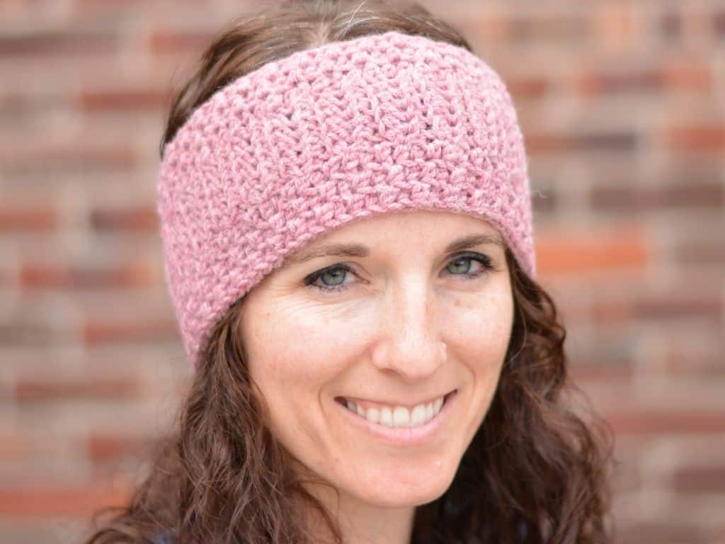 Close up of a young woman with brown curly hair wearing a light pink crochet headband ear warmer