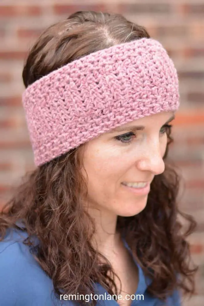 The side view of a brunette wearing a dusty pink crochet ear warmer
