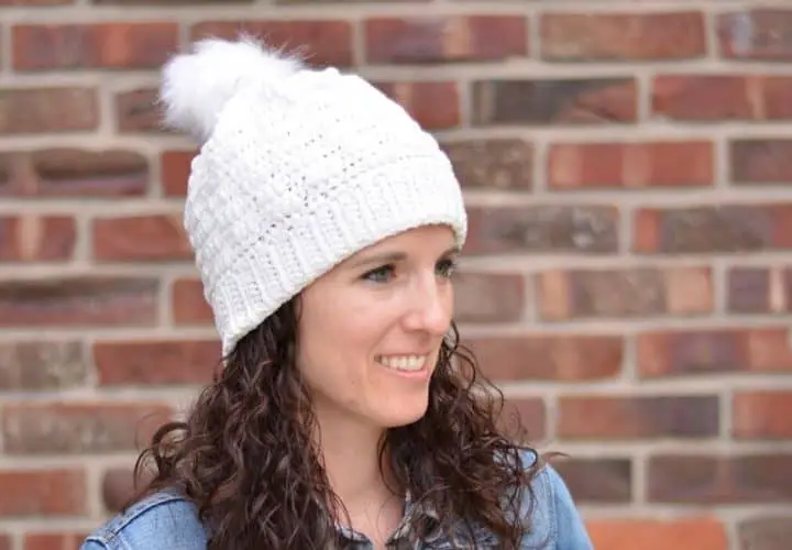 Close-up of a young woman wearing a white crochet winter hat with a white fur pom on top