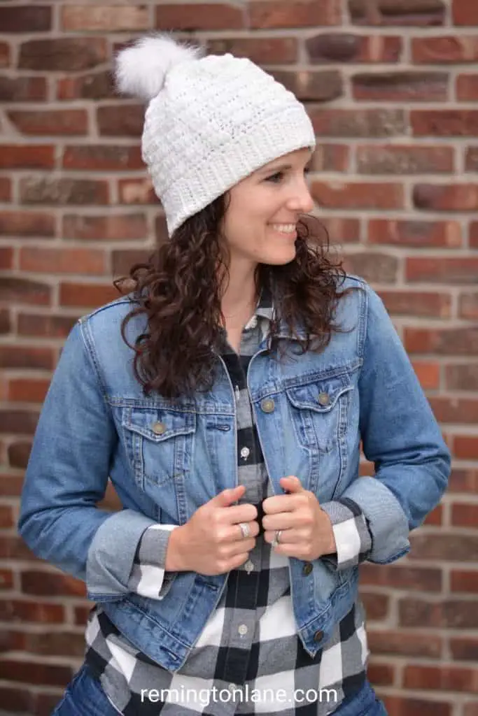 Young woman in a black and white plaid shirt, denim jacket and wearing a white textured crochet winter hat