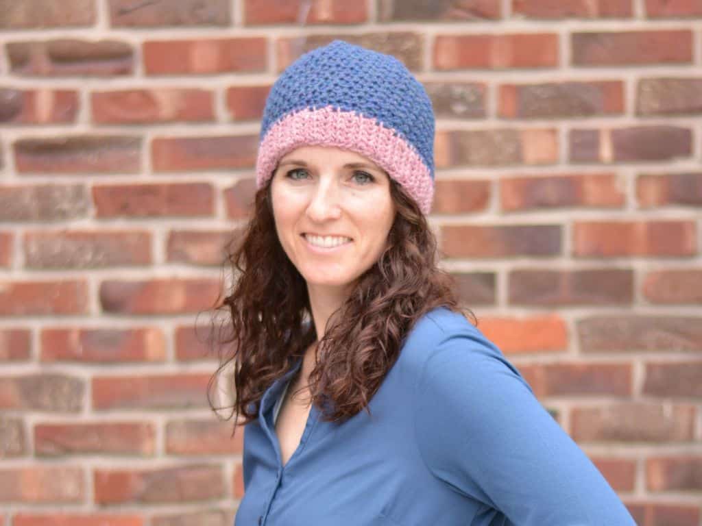A smiling woman wearing a beanie that has been crocheted with blue and pink yarn