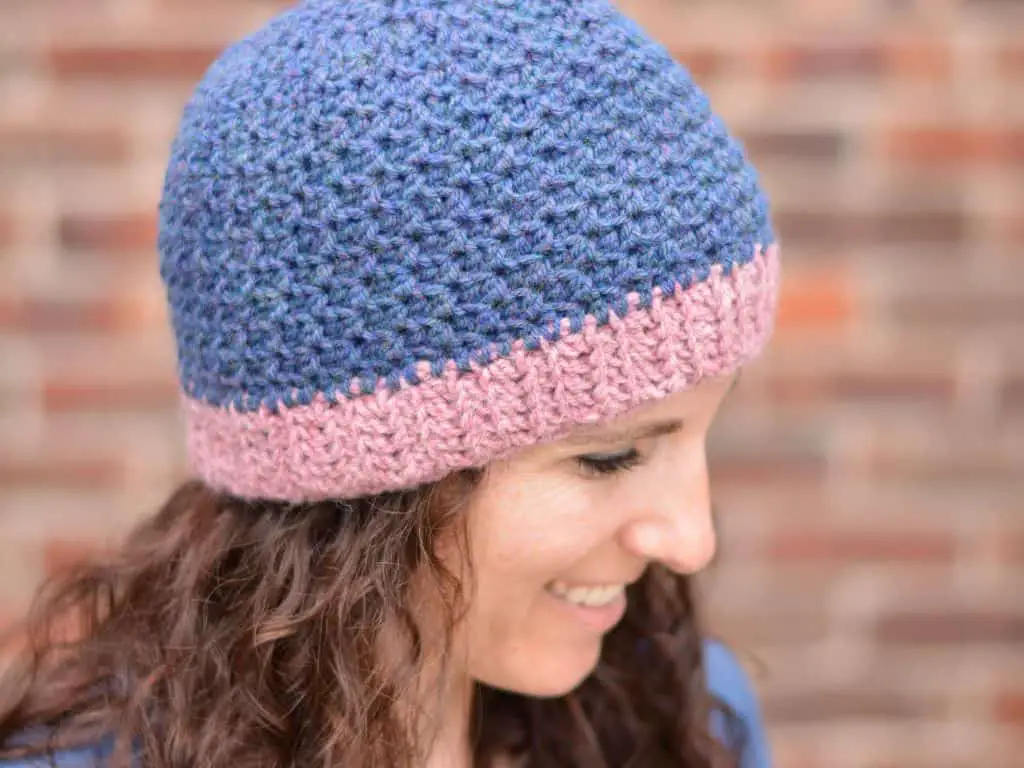 A side view of a woman wearing a deep blue crochet beanie with a heather pink brim.