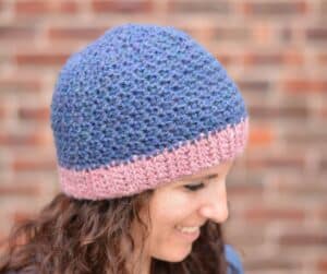Side view of a smiling woman wearing a blue crochet beanie with a pink brim.