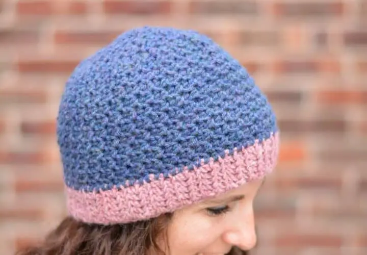 Side view of a smiling woman wearing a blue crochet beanie with a pink brim.