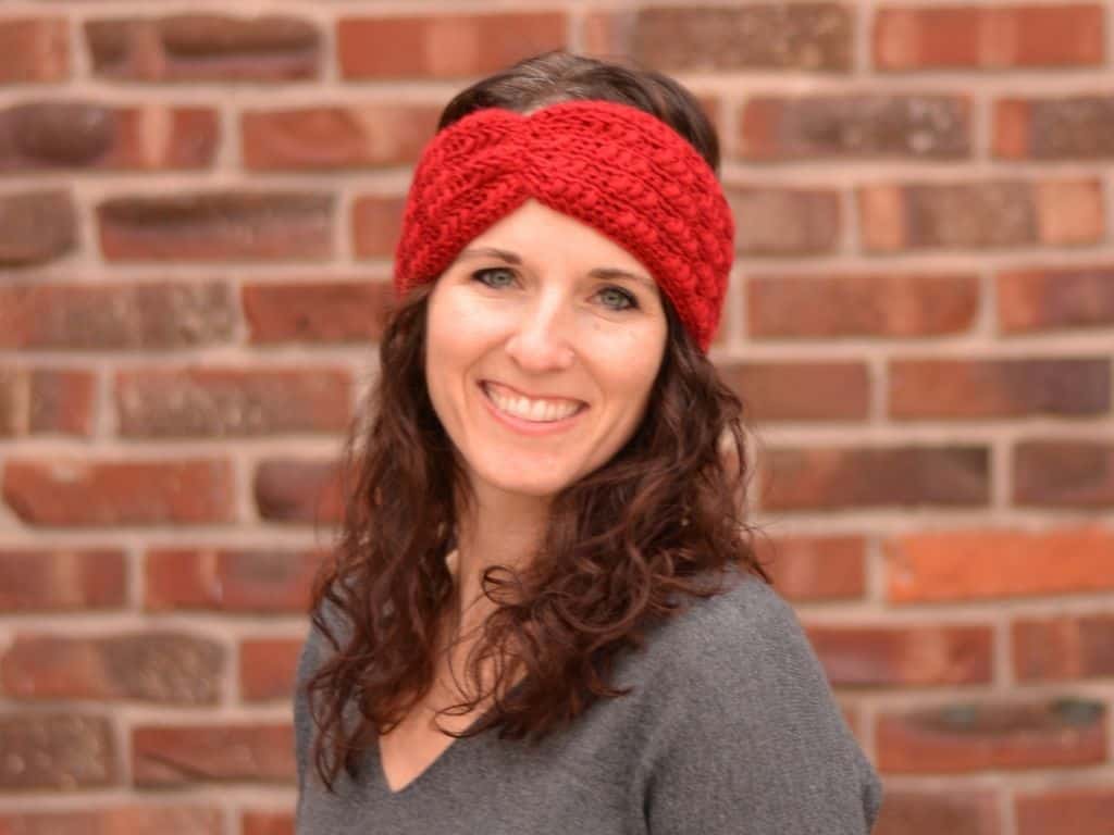 A smiling young woman wearing a bright red crocheted winter ear warmer