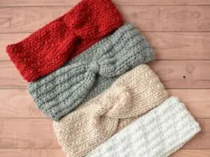 Four crochet ear warmers in different colors lined up on a table