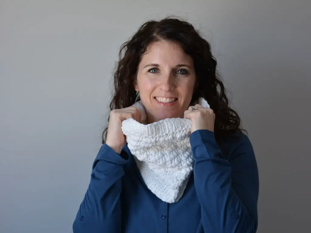 A smiling women cozying up with white crochet cowl.
