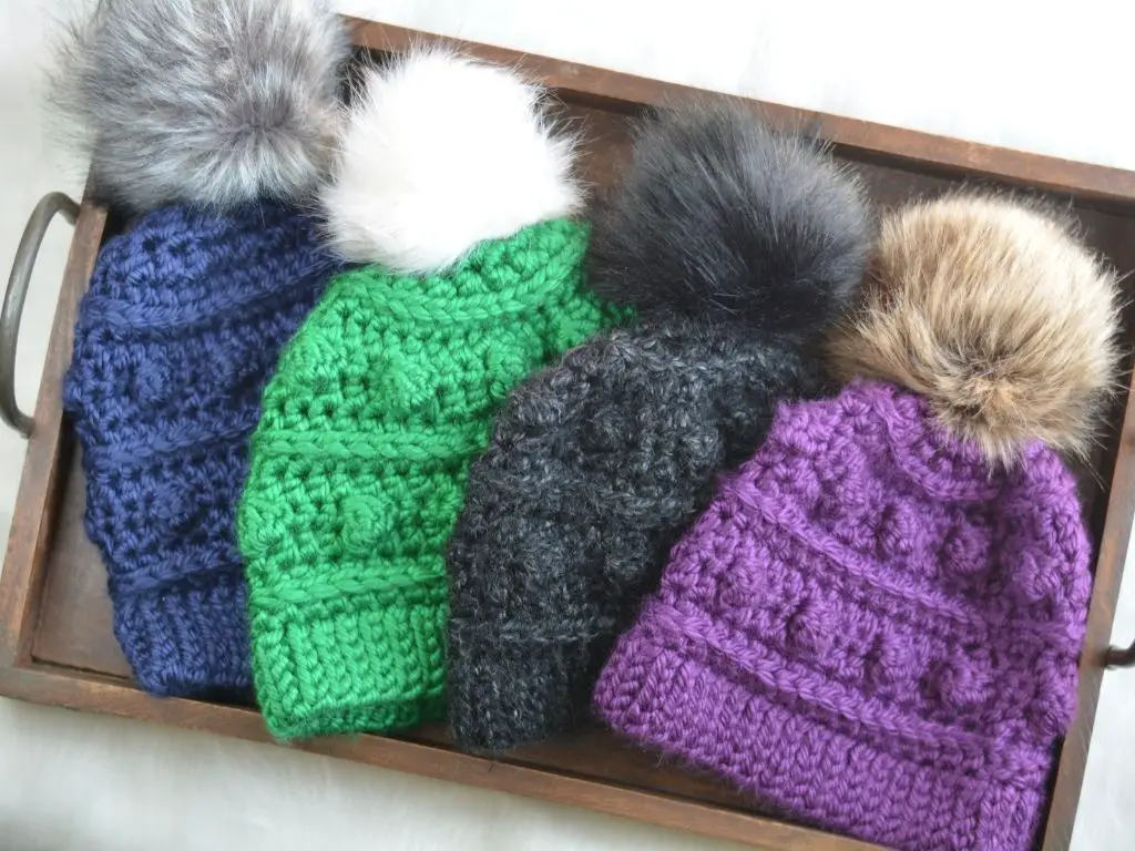 A wooden tray filled with four crochet hats