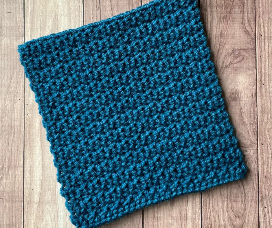 A flat textured square crocheted out of blue yarn on a wooden background