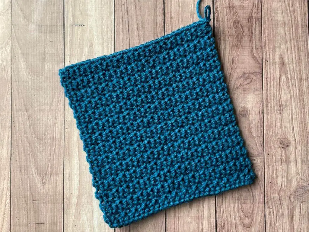 A square made with dark blue yarn laying flat on a wooden table