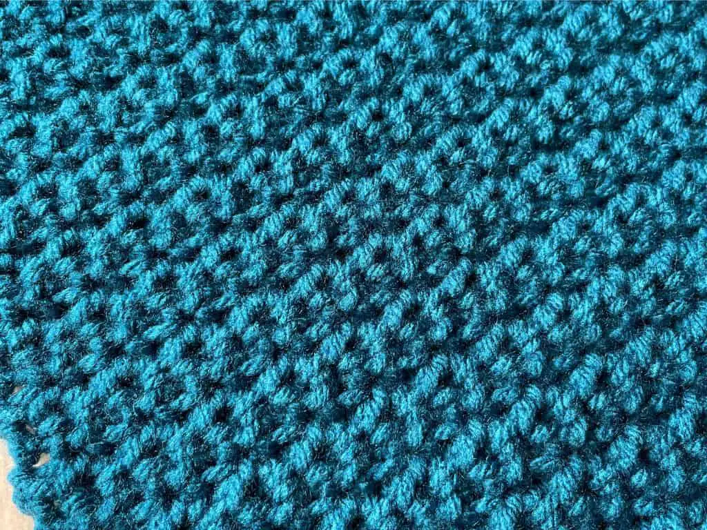 Close up of a square crocheted out of blue yarn