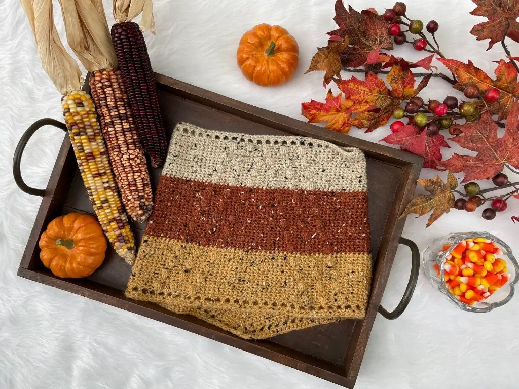 A tablescape decorated for fall with autumn leaves, candy corn, and a crochet cowl laying on a tray