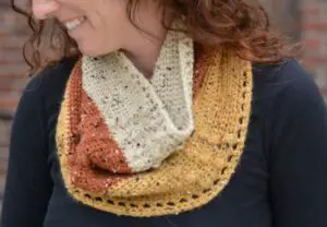A closeup of a fall colored cowl worn by a smiling young woman