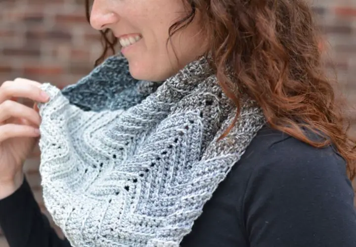 A close-up of a woman wearing a grey ombre crochet cowl