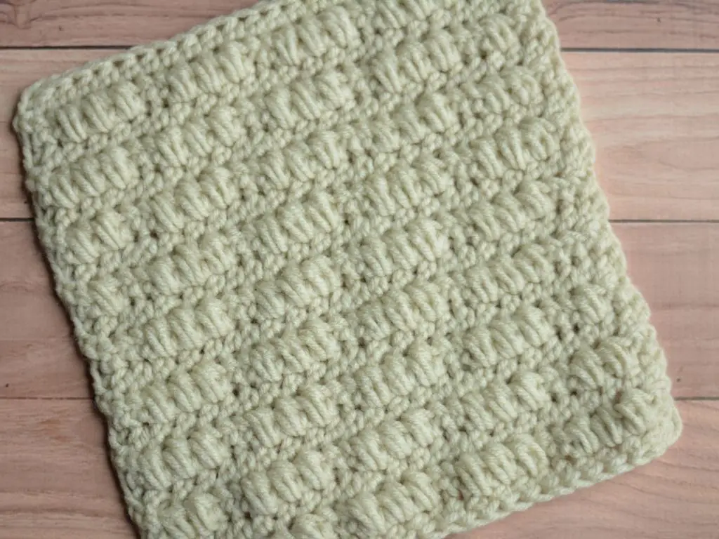 A close-up of a cream crocheted square laying on a wooden table