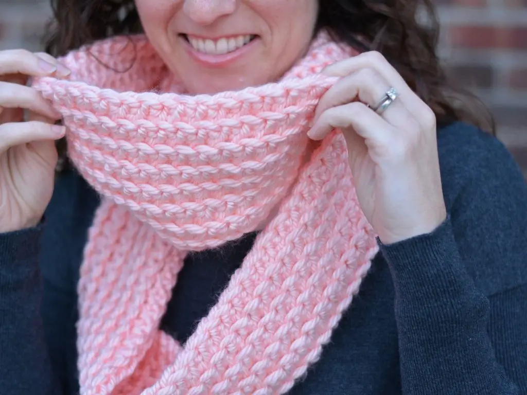 Close up of a woman wearing a light pink crocheted infinity scarf