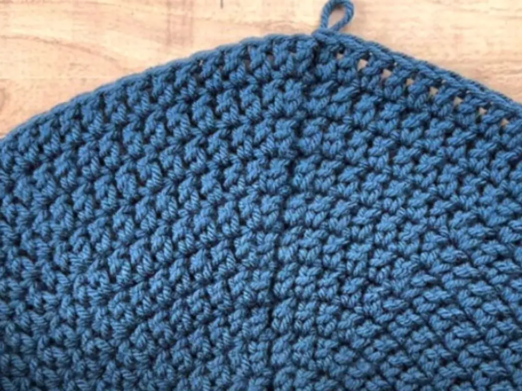 Close up of a flat circle made in blue yarn, laying on a table