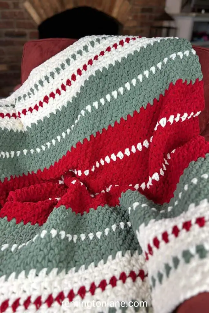 A red, cream, and green striped blanket laying on a red chair in front of a fire place