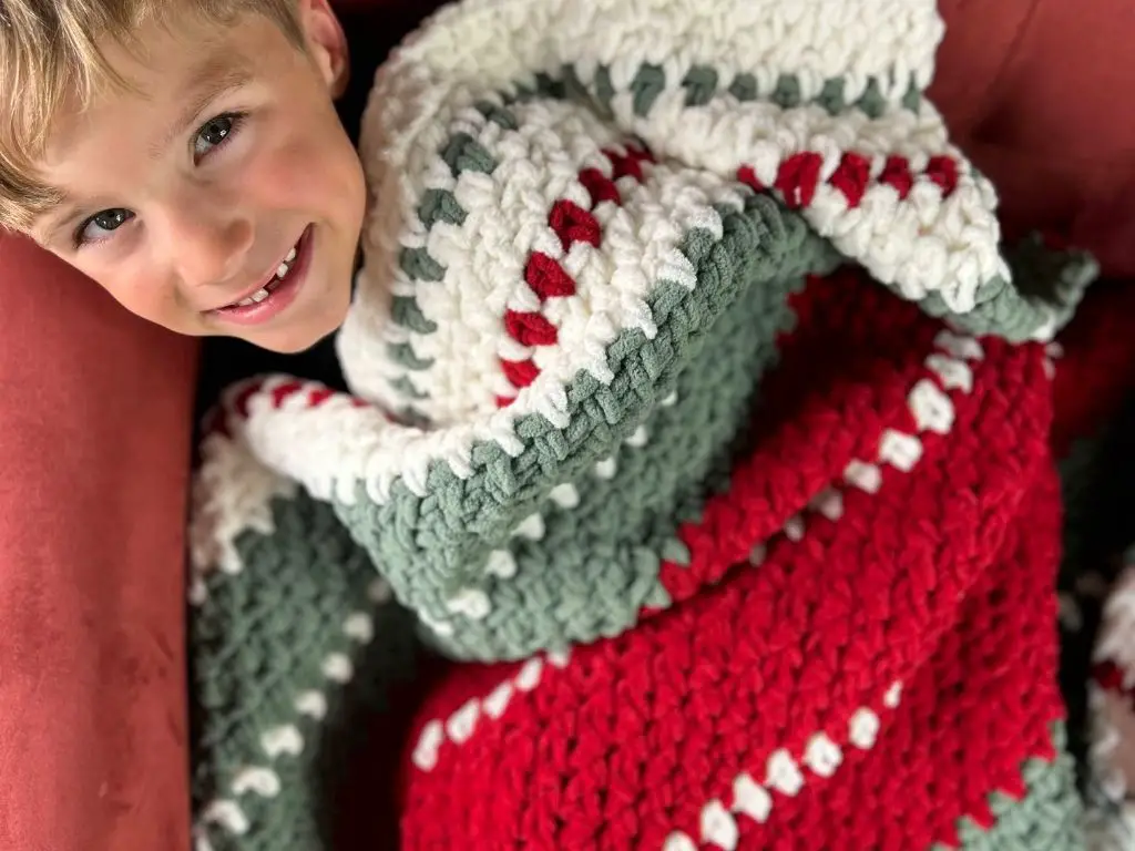 A small boy snuggled up in a Christmas themed striped crochet blanket