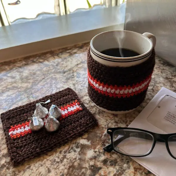 A brown and orange striped coaster with some candy on it next to a mug of coffee 