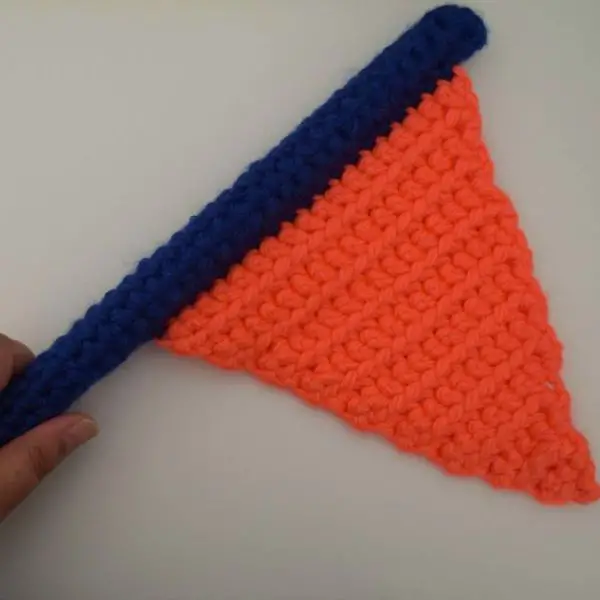 An hand holding an orange flag made out of yarn, with a dark blue flagpole.