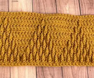 A mustard colored crochet blanket strip with textured triangles on it.