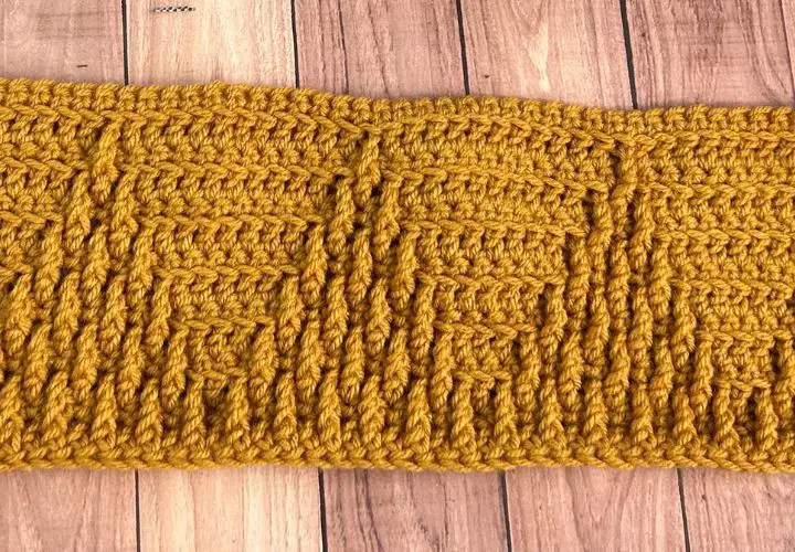 A mustard colored crochet blanket strip with textured triangles on it.