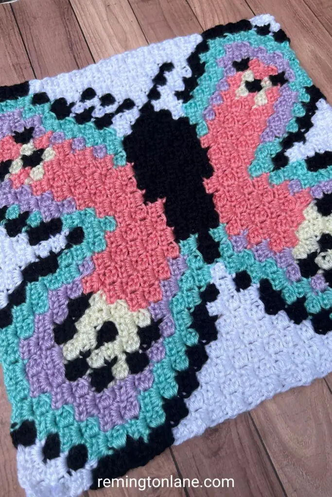A crocheted blanket square made with pastel blue, purple and pink yarn.