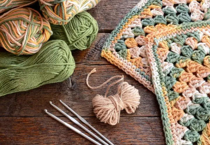 A few crochet hooks, skeins of yarn and blanket squares landing on a table