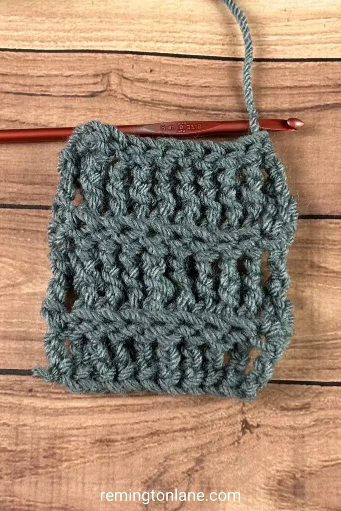 A small grey partially crocheted swatch of back post treble crochet stitches laying on a wooden table.