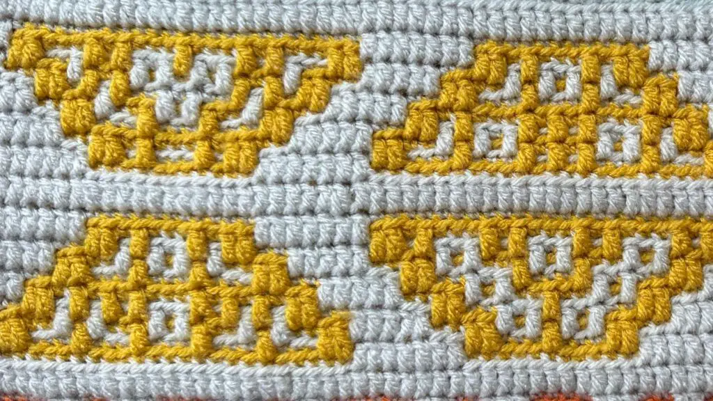 A yellow and white crochet blanket strip that features trapezoid shapes.