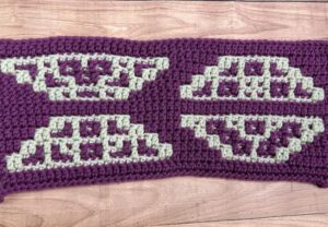 A close up of a trapezoid-themed overlay mosaic crochet section of a blanket made with purple and cream yarn.