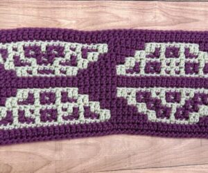 A close up of a trapezoid-themed overlay mosaic crochet section of a blanket made with purple and cream yarn.