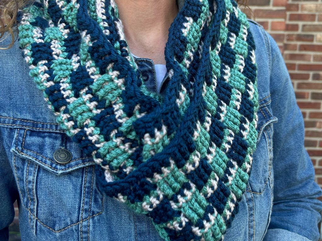 Close-up view of a woman wearing a crocheted infinity scarf made in 3 colors with a basketweave-like pattern