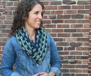 A friendly woman wearing a crocheted infinity scarf in navy, blush and blue-green yarn