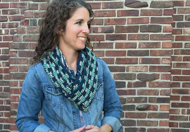 A friendly woman wearing a crocheted infinity scarf in navy, blush and blue-green yarn